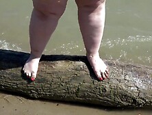 A obese woman with large feet walks along the shore.