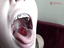 Blue- eyed golden-haired with braces is licking and eating gummy bears in a very hot way