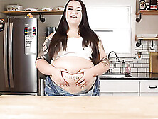 Large dark haired is pridefully showcasing her thick stomach in front of the camera,  in the kitchen