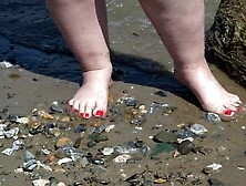 A wide woman with humongous feet walks along the shore.